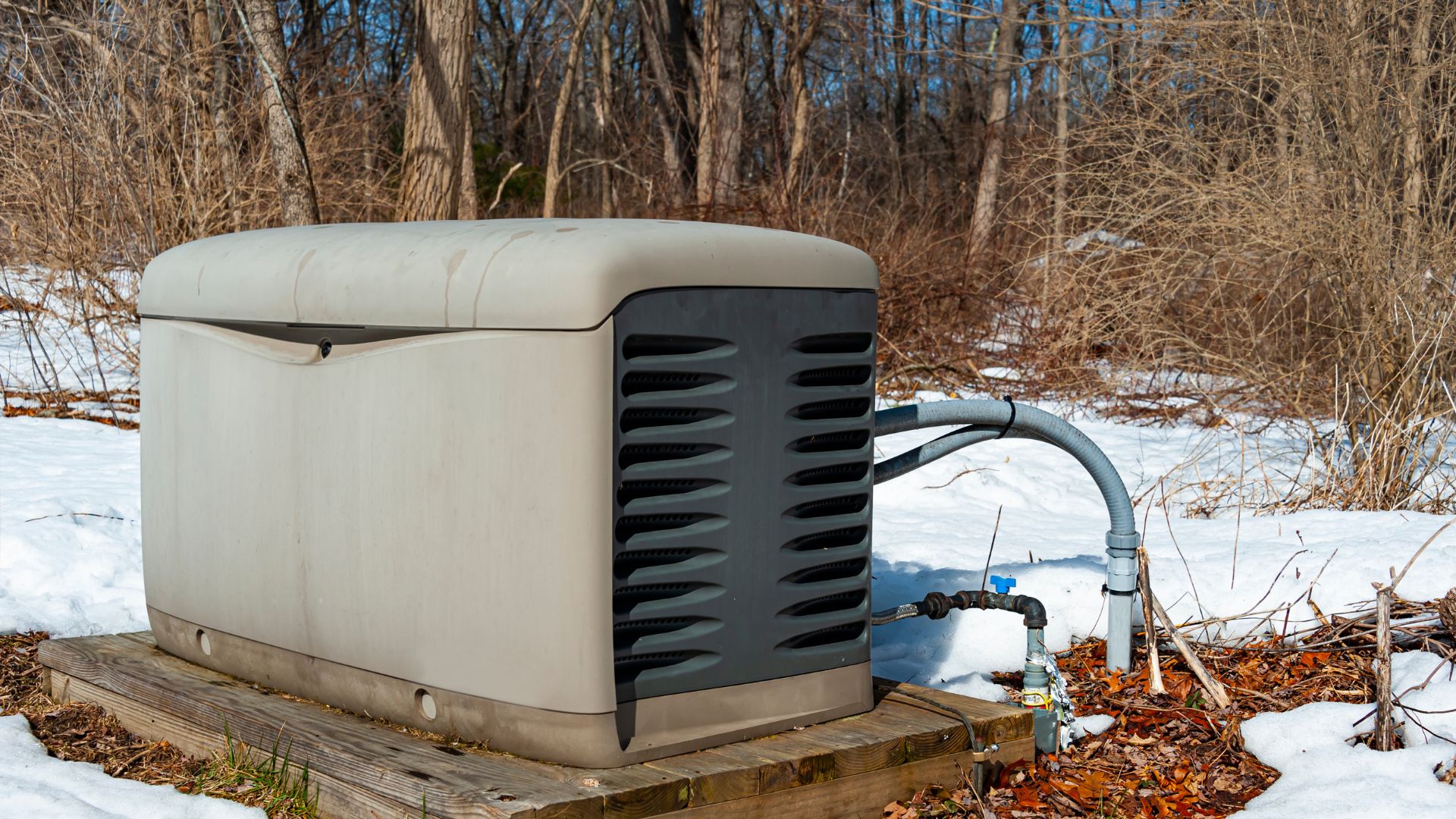 Beige whole-house standby generator with ventilation grilles installed on wooden platform in winter backyard setting