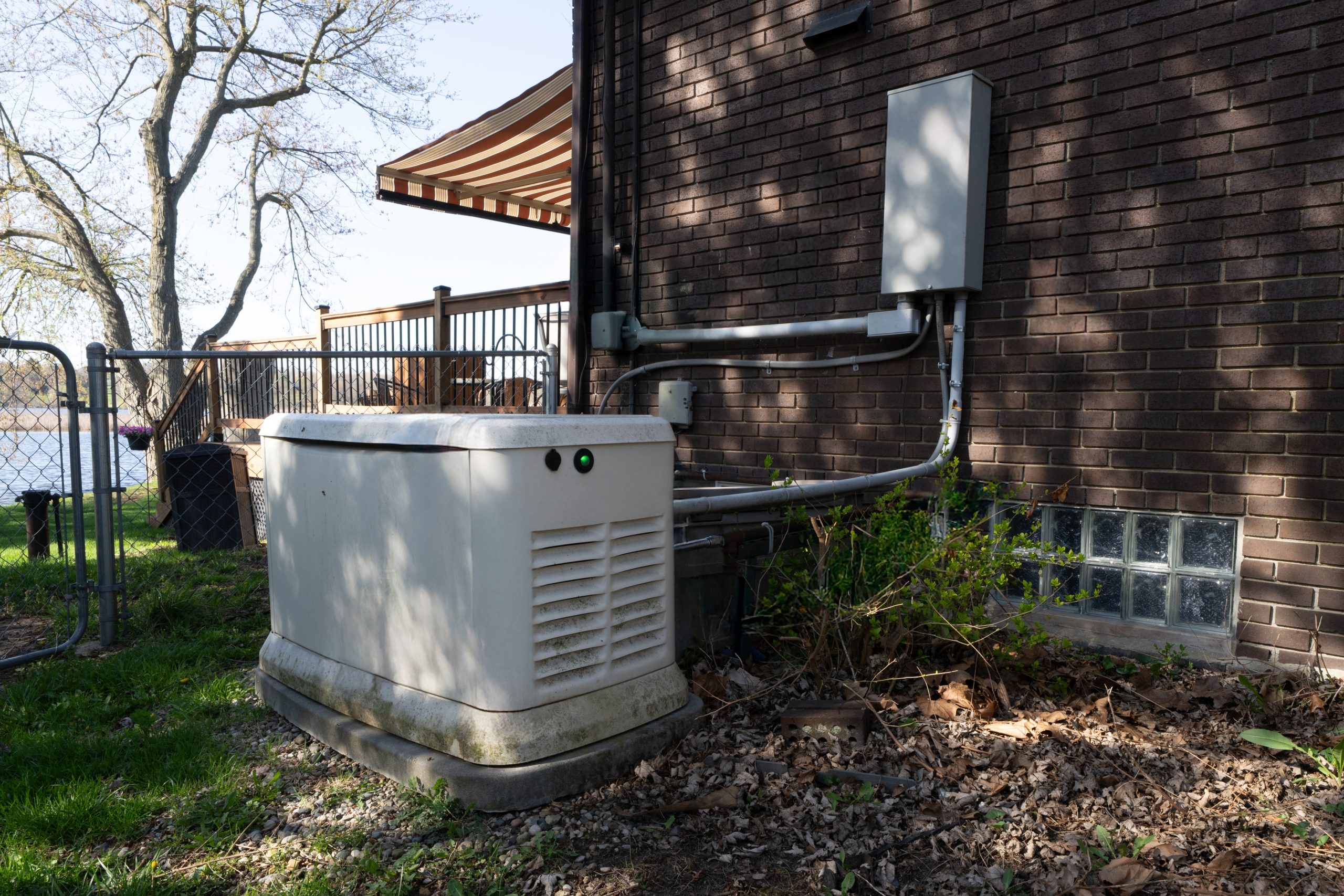A whole house standby generator installed beside a brick home, connected to an electrical panel, illustrating how to choose the right size unit for your house.